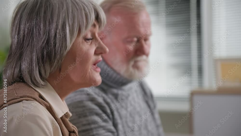 retirees talk and show pills on the webcam of laptop computer, gray-haired grandparents communicate with doctor via the Internet at home, side view retirees talk and show pills on the webcam of laptop computer, gray-haired grandparents communicate with doctor via the Internet at home, side view