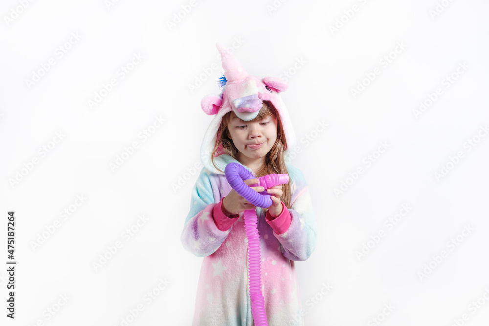 Cheerful little girl in unicorn pajamas plays in a popular toy poptube. An exciting children's game with multi-colored plastic pipes.