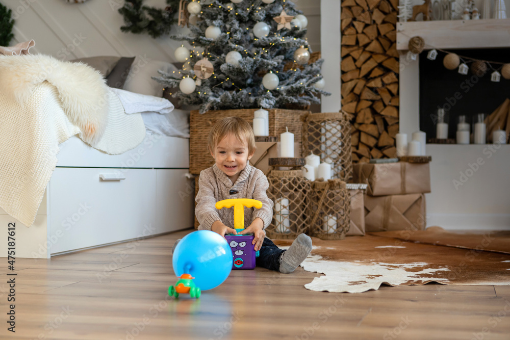 Fototapeta premium A little boy is playing on the floor in a warm sweater and pants