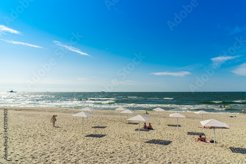 Seascape with clear sky and vacationers on a sandy beach.