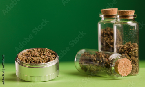 marijuana on grinder, glass jars on table, with dark green background.