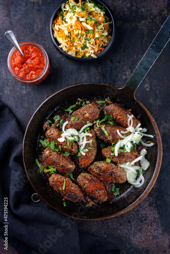 Traditional Croatian cevapcici spicy meat ball rolls with cabbage carrot salad and hot ajvar sauce served as top view in a rustic skillet
