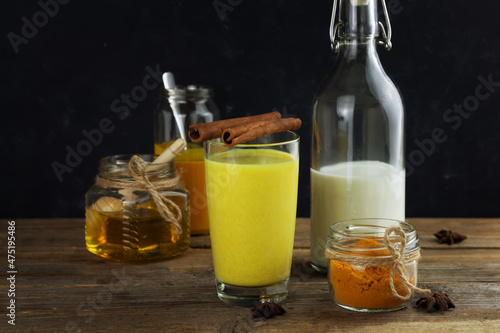 A glass of golden milk, turmeric beverage and ingredients on dark background
