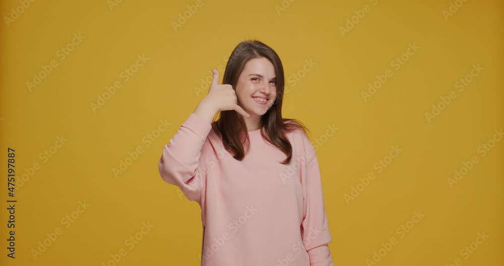 Smiling positive young girl showing call me gesture, pointing finger at camera, flirting on yellow studio background Smiling positive young girl showing call me gesture, pointing finger at camera, flirting on yellow studio background