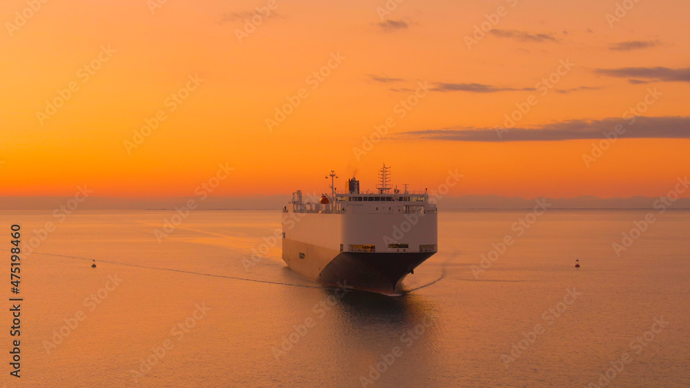 AERIAL: Drone view of a massive cargo carrier sailing across the sea at sunset.