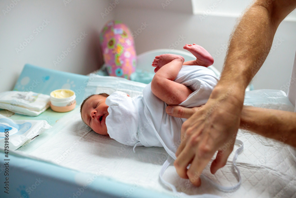 Unrecognizable man changing diapers on a crying newborn baby girl