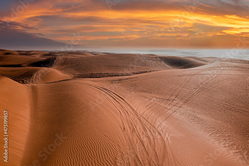 Beautiful sunset over sand dunes with tyre marks at beach against dramatic sky, Fotobehang