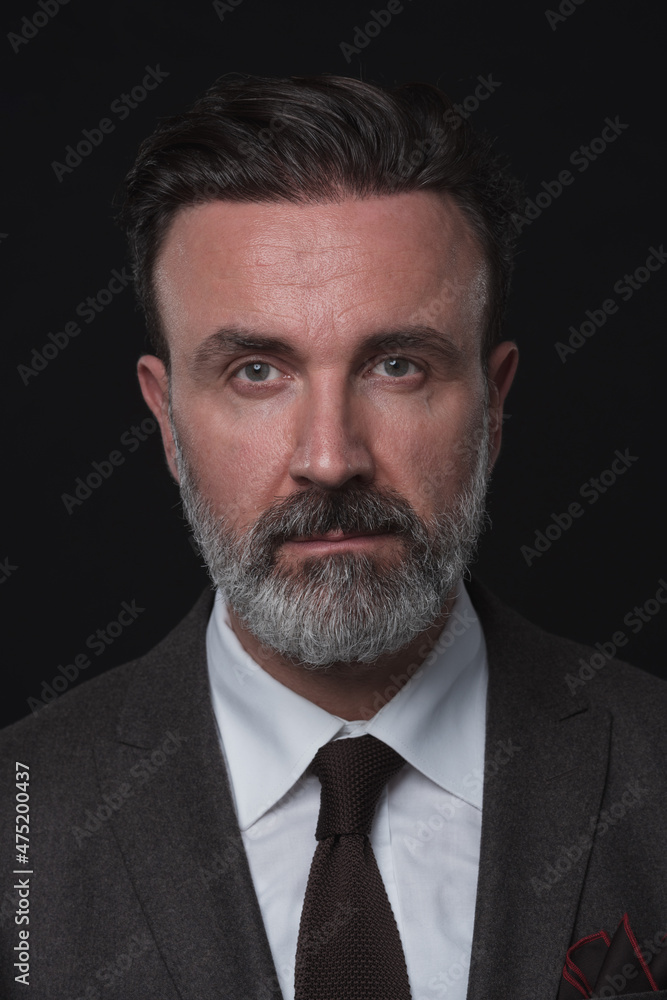 Portrait of a stylish elegant senior businessman with a beard and casual business clothes in photo studio isolated on dark background gesturing with hands Portrait of a stylish elegant senior businessman with a beard and casual business clothes in photo studio isolated on dark background gesturing with hands