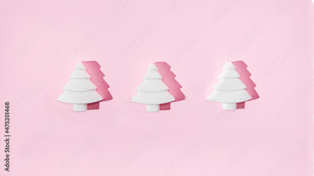 Three geometrical white Christmas trees on pastel pink background. Minimal romantic composition for Christmas or New Year's eve celebration or web banner