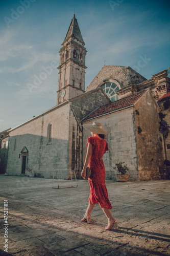 Stylish woman wearing a long red dress and walking around the Catholic church of Saint Nicholas photo