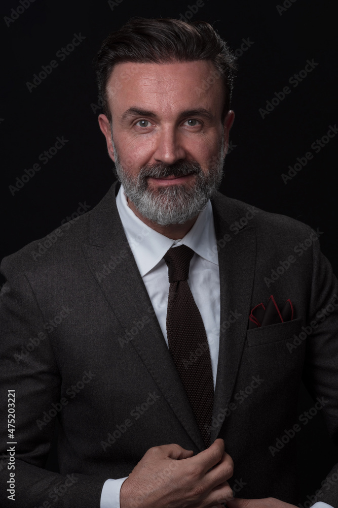 Portrait of a stylish elegant senior businessman with a beard and casual business clothes in photo studio isolated on dark background gesturing with hands Portrait of a stylish elegant senior businessman with a beard and casual business clothes in photo studio isolated on dark background gesturing with hands