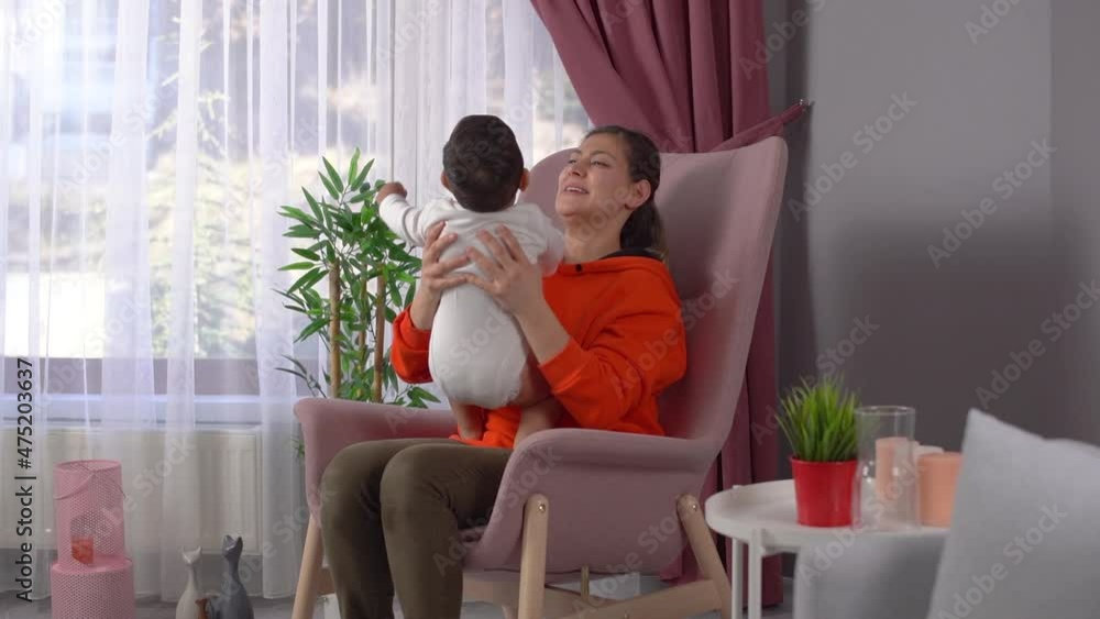 Mother with her baby. The mother sitting in front of the window takes care of her baby in her arms and plays. This is a Slow motion video. Mother with her baby. The mother sitting in front of the window takes care of her baby in her arms and plays. This is a Slow motion video.