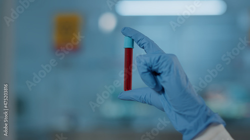 Hand with gloves holding test tube in science laboratory, analyzing dna substance for biology experiment. Microbiology specialist working with glassware and red liquid in flask. Close up