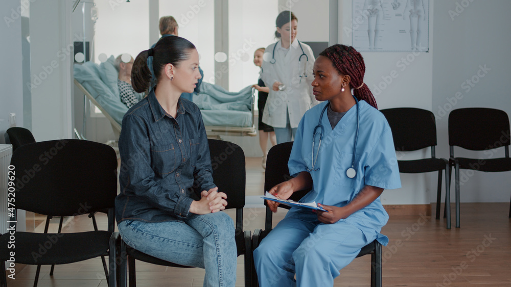 Obraz premium Woman having conversation with nurse in waiting area, talking about diagnosis and healthcare treatment. Medical assistant giving advice and support to patient in waiting room at facility.