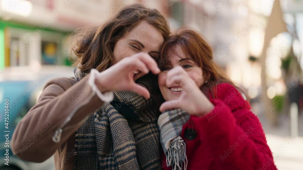 Mother and daughter hugging each other doing heart gesture with hands at street Mother and daughter hugging each other doing heart gesture with hands at street