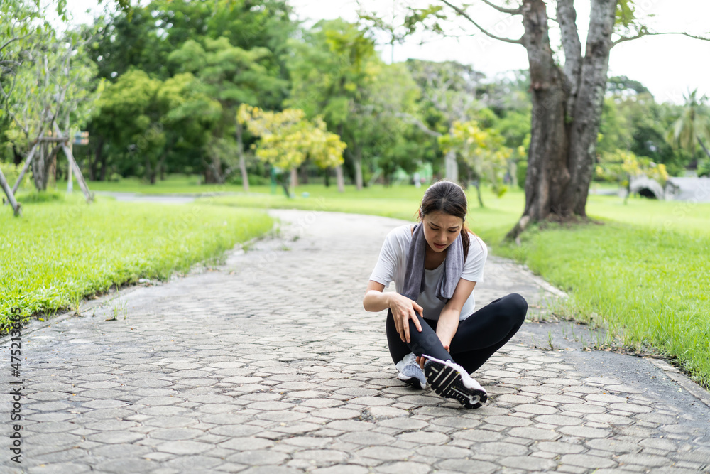 Asian attractive sport woman feels pain on ankle while run on street. Asian attractive sport woman feels pain on ankle while run on street.