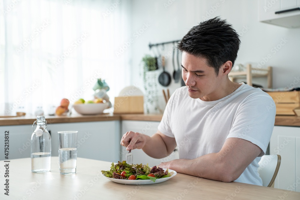 Asian attractive handsome male eating green salad in kitchen at home. Asian attractive handsome male eating green salad in kitchen at home.