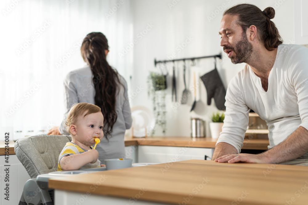 Caucasian beautiful parents take care of baby boy toddler in kitchen. Caucasian beautiful parents take care of baby boy toddler in kitchen.