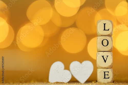 Valentine's Day. Inscription love made of wooden letters and two white hearts on a gold glitter background with gold bokeh. Valentines day background in gold tones.Love and relationship.
