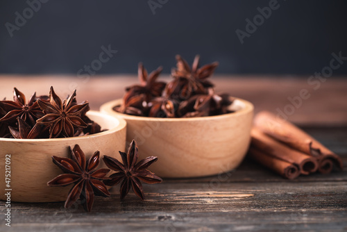 Star anise in bowl and cinnamon stick on wooden background