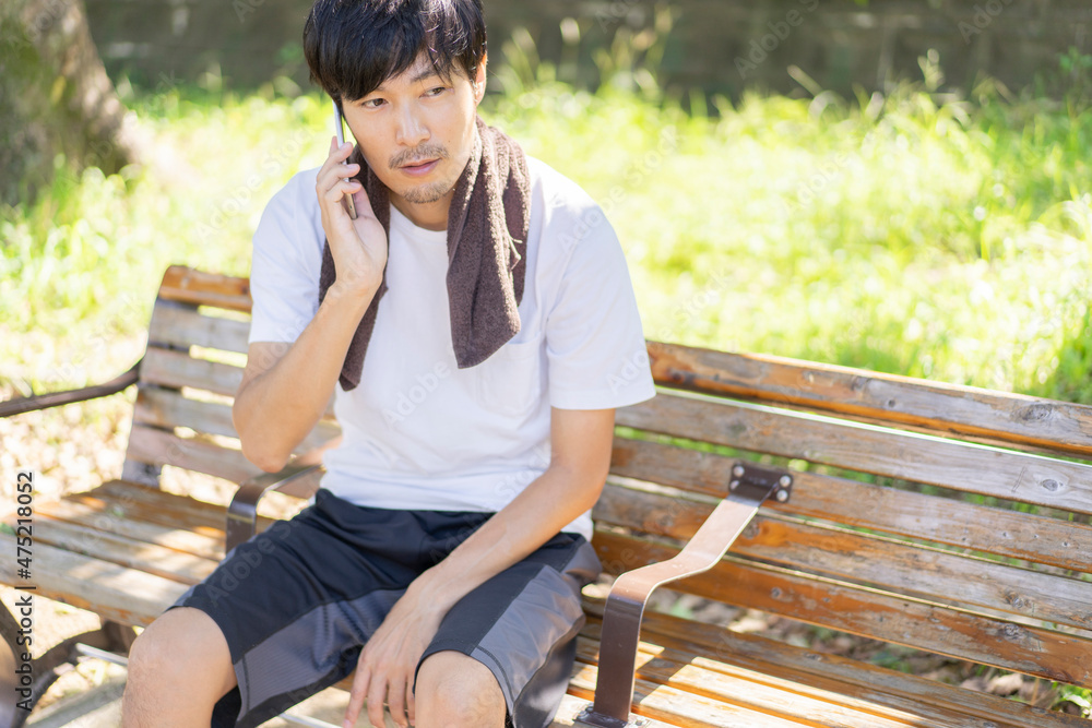ベンチでケータイ電話を触る男性 ベンチでケータイ電話を触る男性