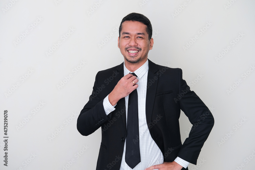 Adult Asian man wearing black suit showing high confidence with hand touching his tie Adult Asian man wearing black suit showing high confidence with hand touching his tie