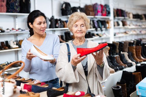 Fototapeta Naklejka Na Ścianę i Meble -  Friendly female sales consultant demonstrates ballet flats to a mature woman customer who came to a shoe store for shopping