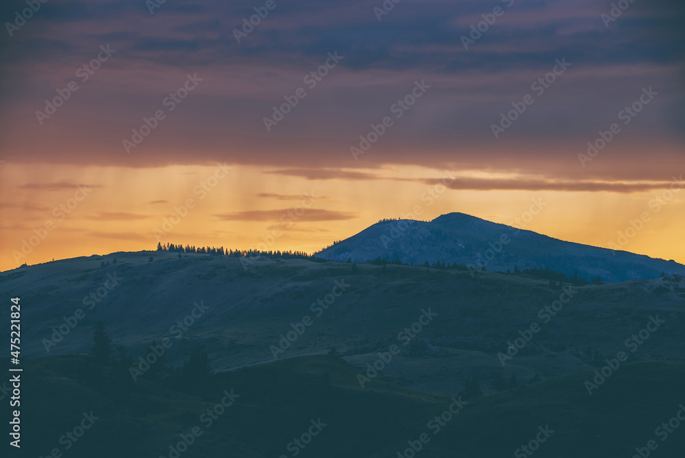 Atmospheric landscape with silhouettes of mountains with trees on background of vivid orange blue lilac dawn sky. Colorful nature scenery with sunset or sunrise of illuminating color. Sundown paysage. Atmospheric landscape with silhouettes of mountains with trees on background of vivid orange blue lilac dawn sky. Colorful nature scenery with sunset or sunrise of illuminating color. Sundown paysage.