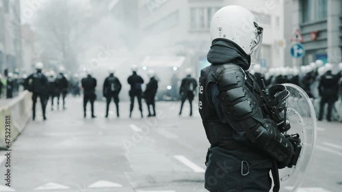 Cinematic shot of unrecognizable police officer in full gear protecting the street with his unit during riots photo