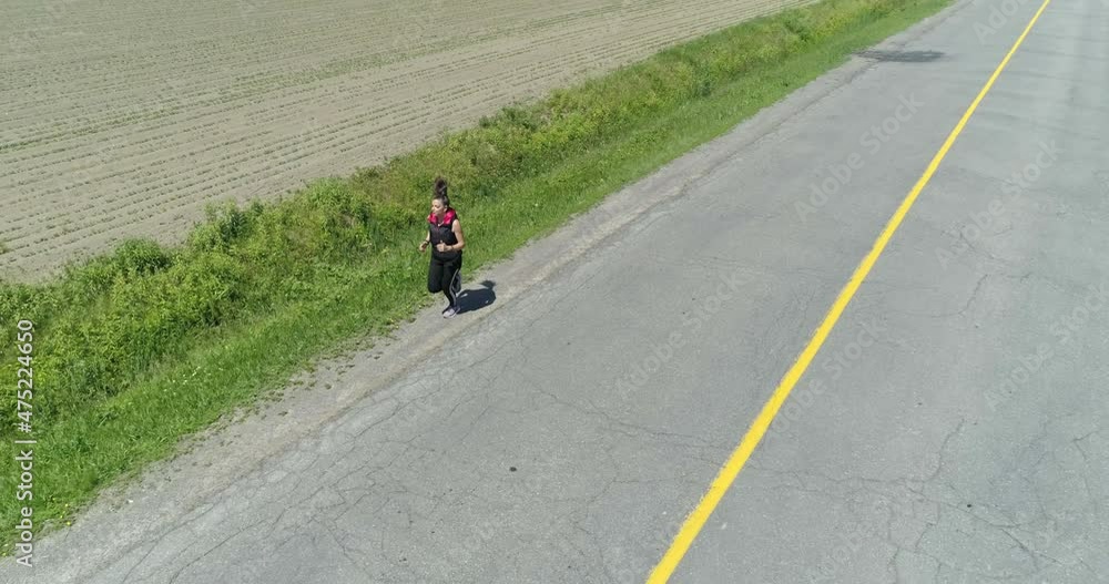 Drone flying backward in front of a woman jogging in a very long road in the country Drone flying backward in front of a woman jogging in a very long road in the country