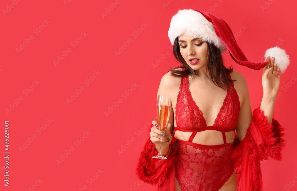 Sexy young woman in Santa hat and underwear drinking champagne on color background Sexy young woman in Santa hat and underwear drinking champagne on color background