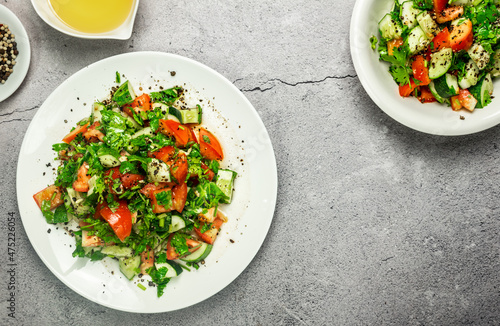 Lazy mediterranean salad with tomatoes, cucumber, coriander, onions, olive oil and lemon in a white ceramic plate selective focus. Healthy vegetarian food, oriental and Mediterranean cuisine. Top view