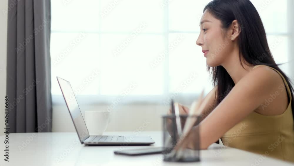 Beautiful asian woman using laptop chatting video conference online sitting in living room at home. Business Woman looking at screen Meeting on social media. Work from home. Beautiful asian woman using laptop chatting video conference online sitting in living room at home. Business Woman looking at screen Meeting on social media. Work from home.