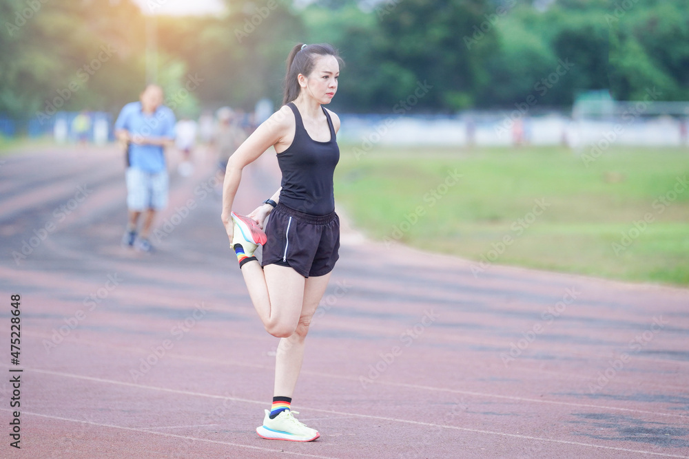 A mature beautiful Asian woman in sports outfits stretching before workout outdoor in the city stadium park in the morning to get a healthy lifestyle. Healthy young woman warming up outdoors A mature beautiful Asian woman in sports outfits stretching before workout outdoor in the city stadium park in the morning to get a healthy lifestyle. Healthy young woman warming up outdoors