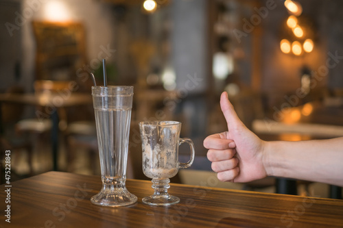 Two empty iced coffee glass cups on the table in coffee shop and hand showing thumbs up sign. High quality photo