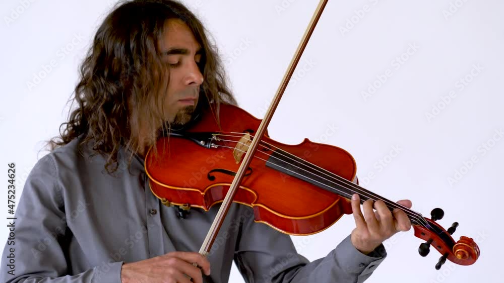 Medium shot of long hair ethnic male musician in grey button up shirt practicing music on red viola Medium shot of long hair ethnic male musician in grey button up shirt practicing music on red viola