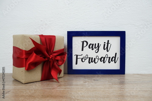 Pay it forward typography text and gift box on wooden table and white wall background