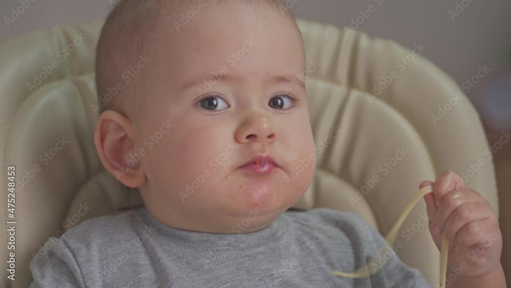 Toddler independently eats spaghetti with his hands while sitting on a feeding chair. Closeup Toddler independently eats spaghetti with his hands while sitting on a feeding chair. Closeup