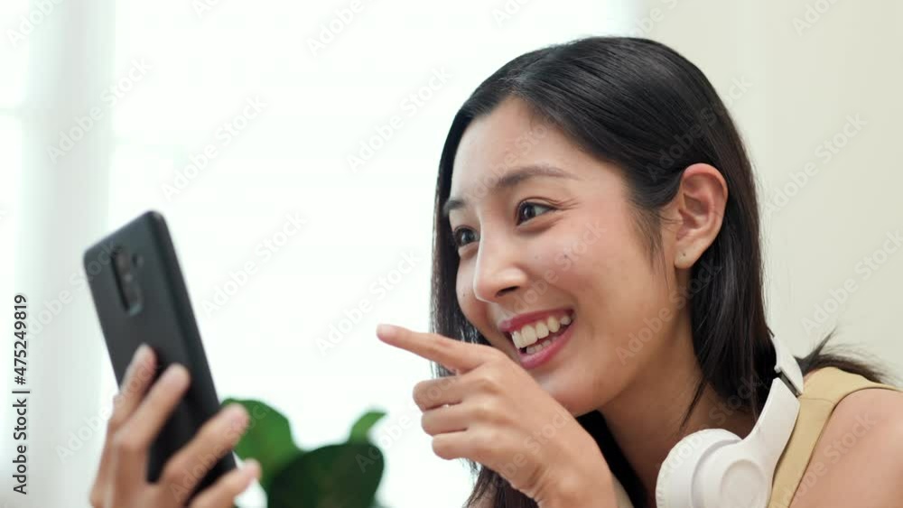 Asian woman using smartphone chatting video conference online sitting sofa in living room at home. Business Woman looking at screen Meeting on social media. Relax time at home Asian woman using smartphone chatting video conference online sitting sofa in living room at home. Business Woman looking at screen Meeting on social media. Relax time at home
