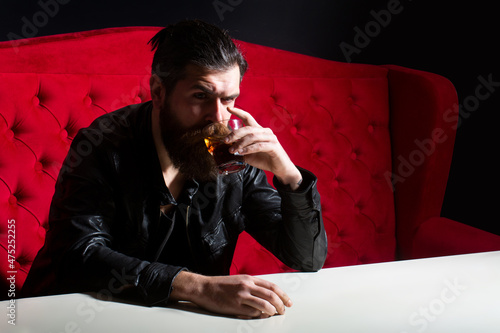 Bearded man drinking whisky, whiskey or cognac brandy. Hipster brutal man drinker alcoholic with alcoholism problem, alcohol abuse addiction concept. Drunken man behavior. photo