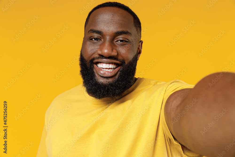 Close up young fun smiling happy black man 20s wearing bright casual t-shirt doing selfie shot pov on mobile phone isolated on plain yellow color background studio portrait. People lifestyle concept. Close up young fun smiling happy black man 20s wearing bright casual t-shirt doing selfie shot pov on mobile phone isolated on plain yellow color background studio portrait. People lifestyle concept.