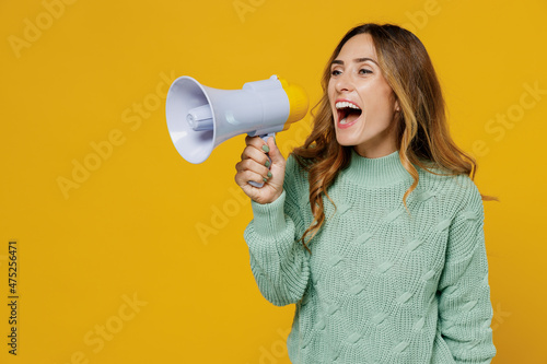 Young expressive woman 30s wear green knitted sweater hold scream in megaphone announces discounts sale Hurry up isolated on plain yellow color background studio portrait. People lifestyle concept.