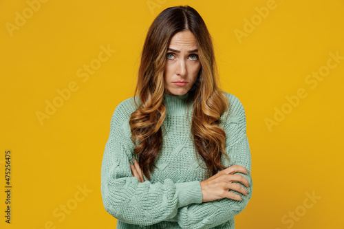 Young offended shrewd woman 30s wearing green knitted sweater look camera hold hands crossed folded looking camera isolated on plain yellow color background studio portrait. People lifestyle concept.