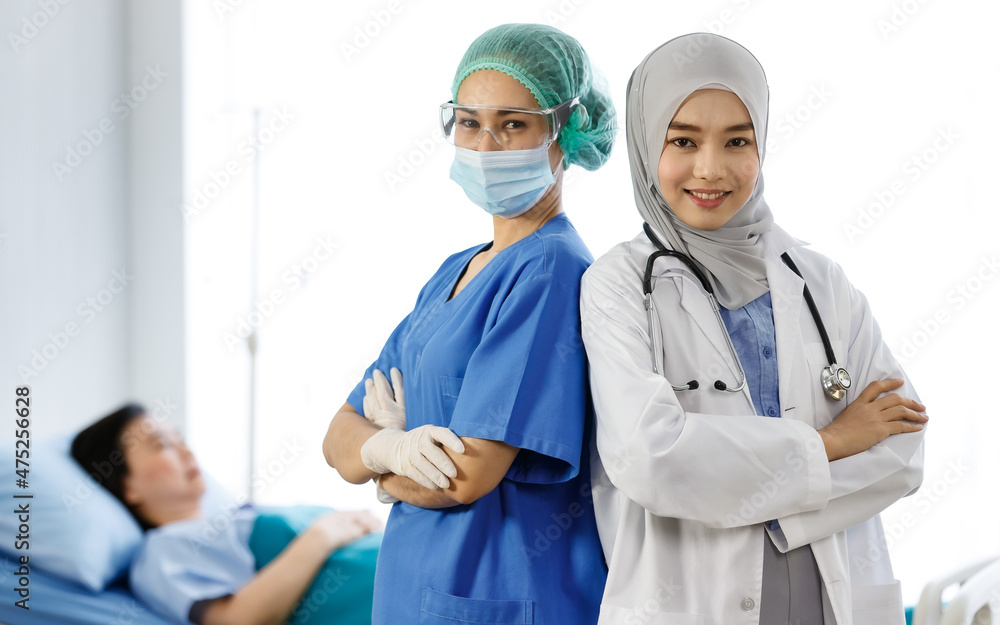 Portrait shot of Muslim Islam Arab doctor in hijab white lab coat with stethoscope and Asian female nurse in blue hospital uniform with face mask and goggles crossed arms stand leaning back together Portrait shot of Muslim Islam Arab doctor in hijab white lab coat with stethoscope and Asian female nurse in blue hospital uniform with face mask and goggles crossed arms stand leaning back together