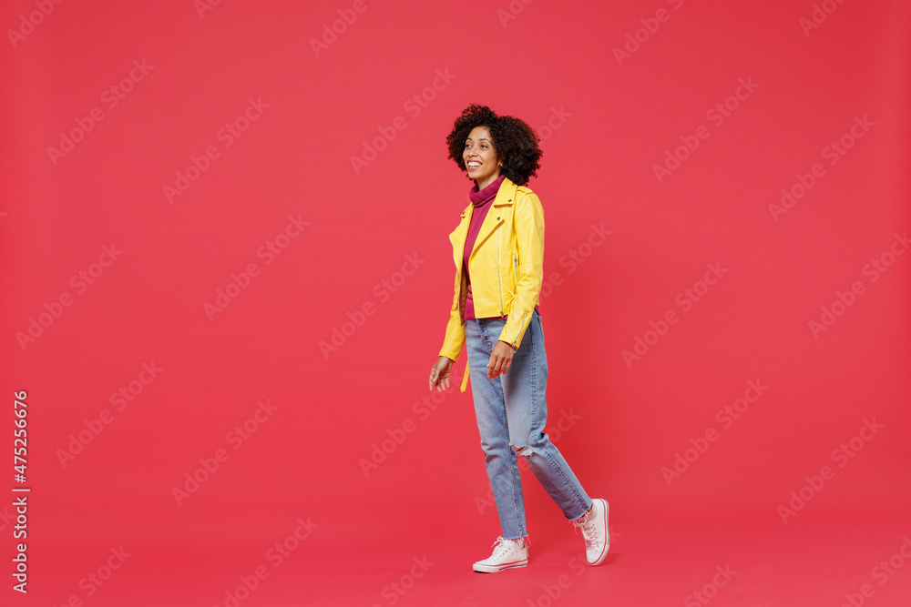 Full size body length bright fascinating happy fun bright young curly black latin woman 20s years old wears yellow jacket go move stroll looking aside isolated on plain red background studio portrait. Full size body length bright fascinating happy fun bright young curly black latin woman 20s years old wears yellow jacket go move stroll looking aside isolated on plain red background studio portrait.