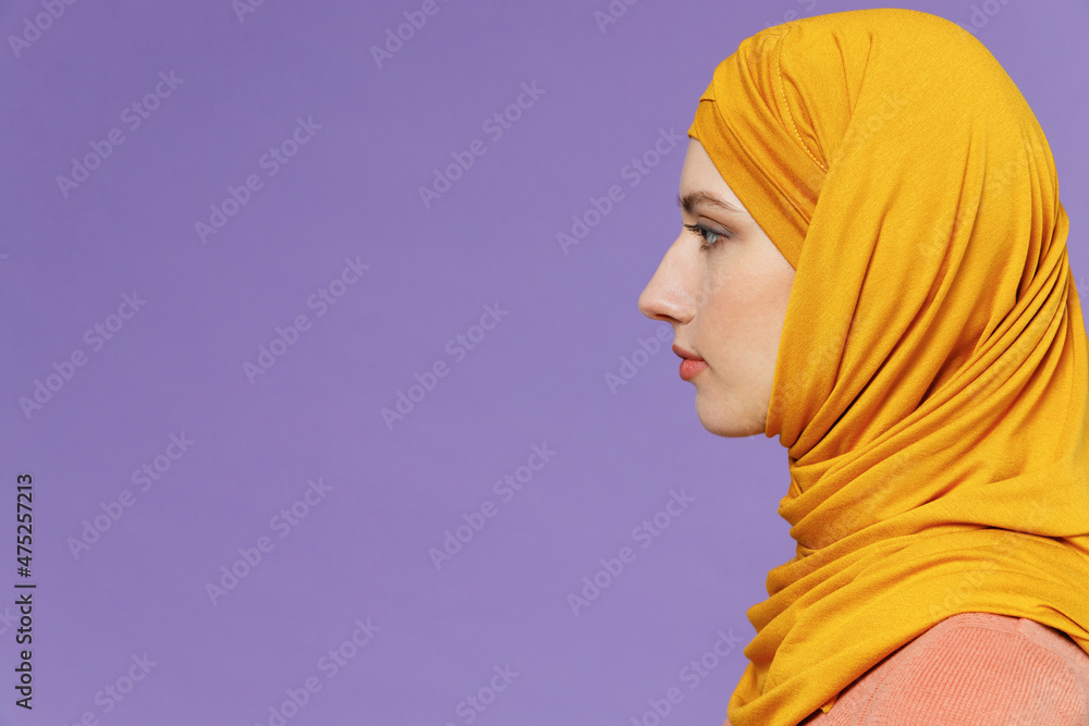 Fototapeta premium Side view severe sad young arabian asian muslim woman in abaya hijab yellow clothes isolated on plain pastel light violet background studio portrait. People uae middle eastern islam religious concept.