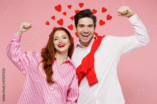 Young smiling couple two friends woman man in casual shirt look camera do winner gesture clench fist isolated on plain pink background studio portrait. Valentine's Day birthday holiday party concept.