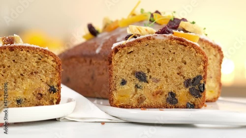 Close-up. A sliced fruitcake soaked in rum is on the table. Christmas atmosphere with lanterns in the background. Christmas homemade muffin. Traditional cupcake with dried fruits. Camera movement.