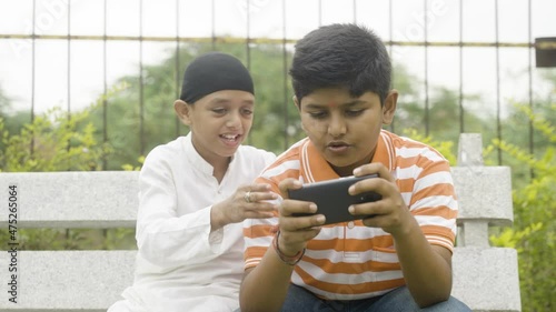 Multiethnic kids playing video game on mobile phone at park - concept of technology, smartphone addiction, friendship and leisure activities photo