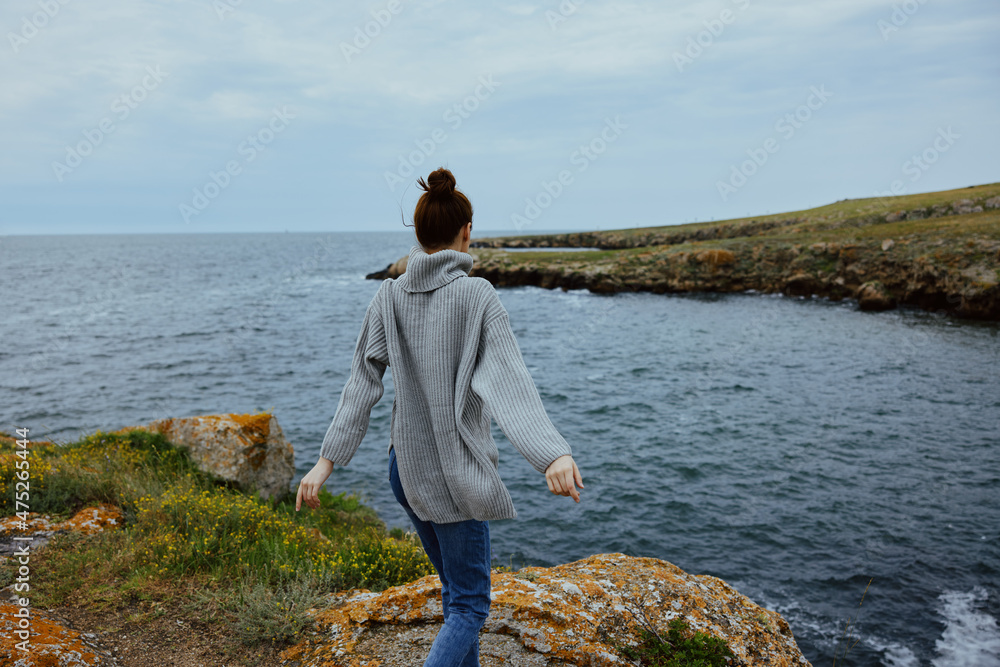 beautiful woman in a gray sweater stands on a rocky shore nature Relaxation concept